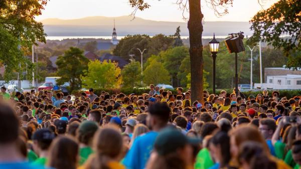 A sea of students outside on UVM's campus with Lake Champlain and the Adirondack mountains in the background